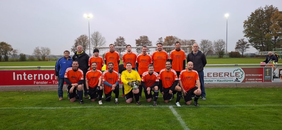 Die Alten Herren in orangefarbenen Trikots mit Betreuern auf einem Sportplatz