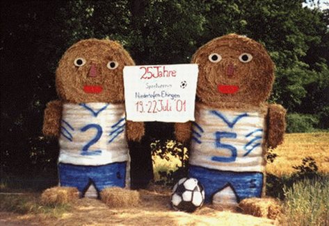 Zwei Strohballenfiguren in blau-weißen Trikots mit den Rückennummern 2 und 5, dazwischen ein Schild zum 25-jährigen Jubiläum des Sportvereins Niederhofen-Ehingen im Juli 2001