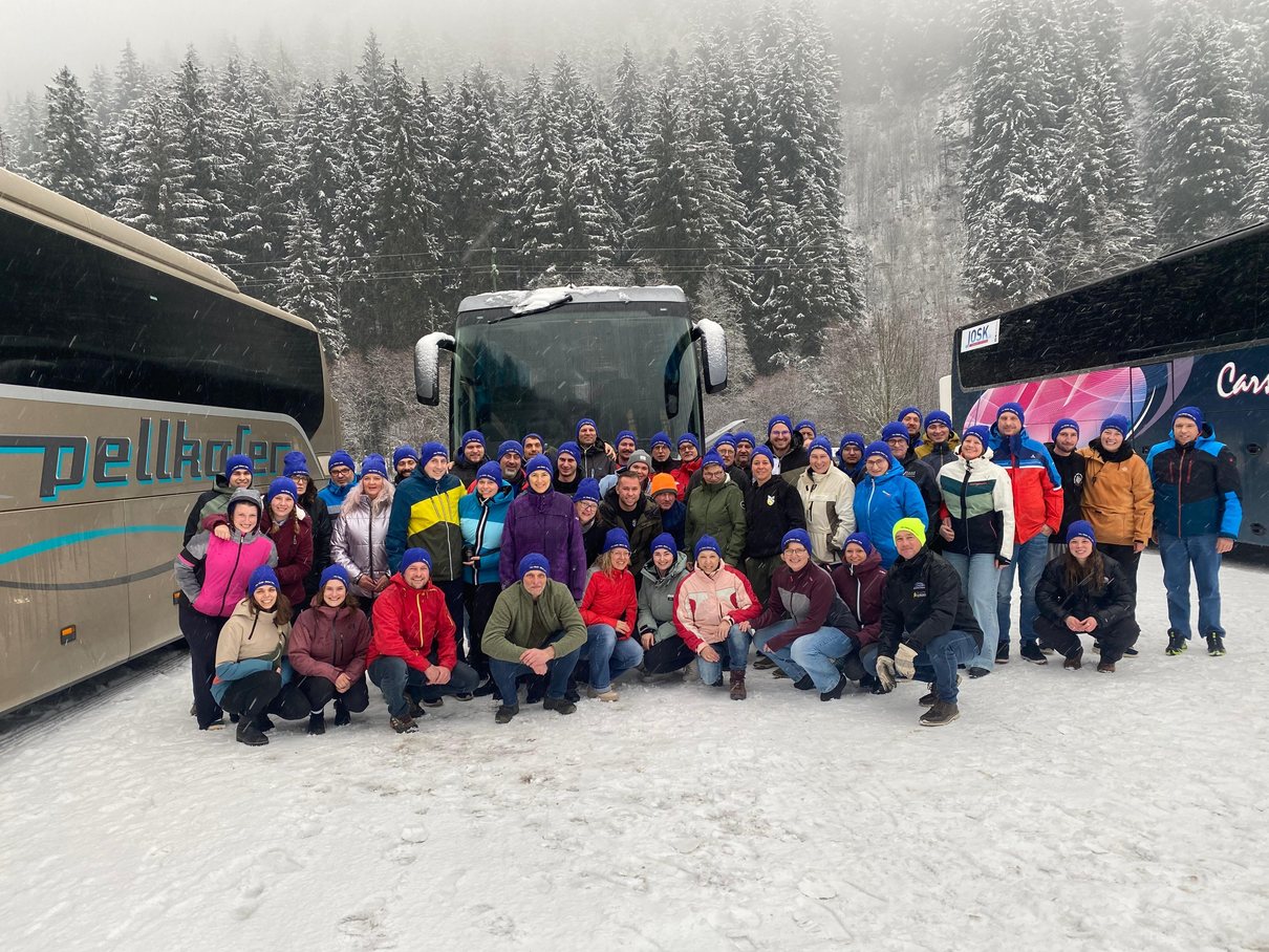Große Reisegruppe mit bunten Mützen im Schnee vor Reisebussen