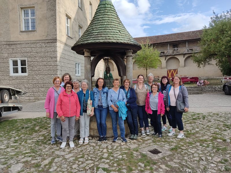 Gruppe der Damengymnastik vor einem Brunnen mit Holzdach in einem Burghof