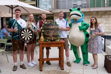Gruppe in Tracht mit Dartscheibe, Bierfass und einem Frosch-Maskottchen