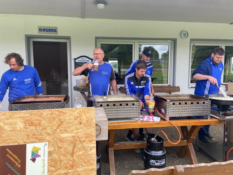 Helfer in blauen Vereinsshirts an großen Grillplatten