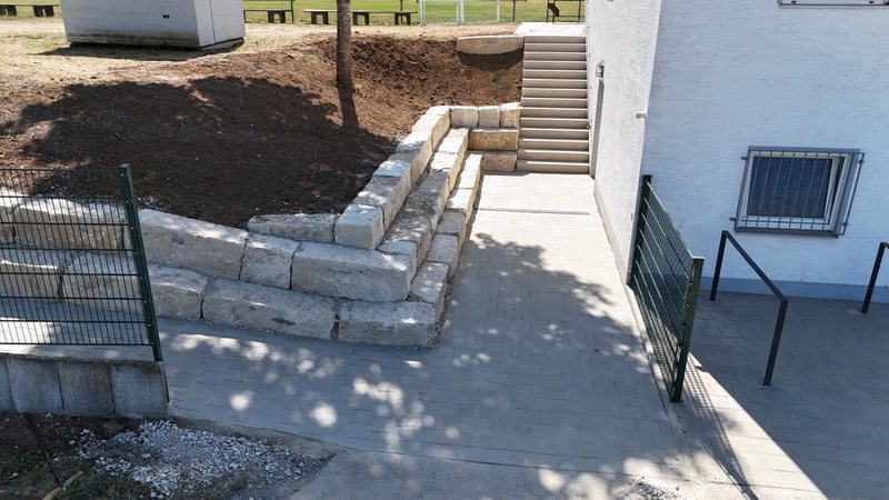 Natursteinmauer mit Stufen und gepflasterter Fläche direkt am Sportheim