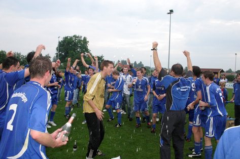 Spieler in blauen Trikots jubeln mit erhobenen Armen auf dem Rasen