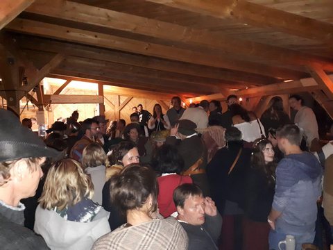 Dicht besetzte Bänke unter einem Holzdach am Abend