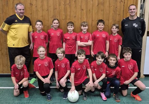 E-Jugend in roten Trikots mit zwei Trainern in der Halle