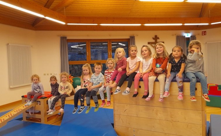 Kinder sitzen nebeneinander auf einem Turnkasten in einer Halle