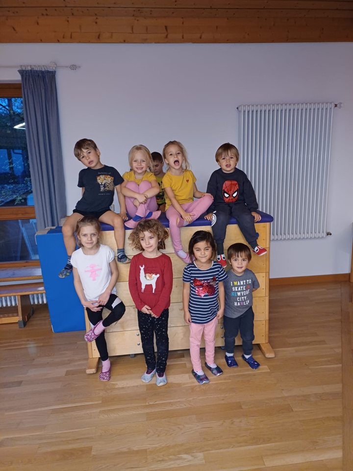 Kinder stehen und sitzen auf einem Turnkasten in einem hellen Raum