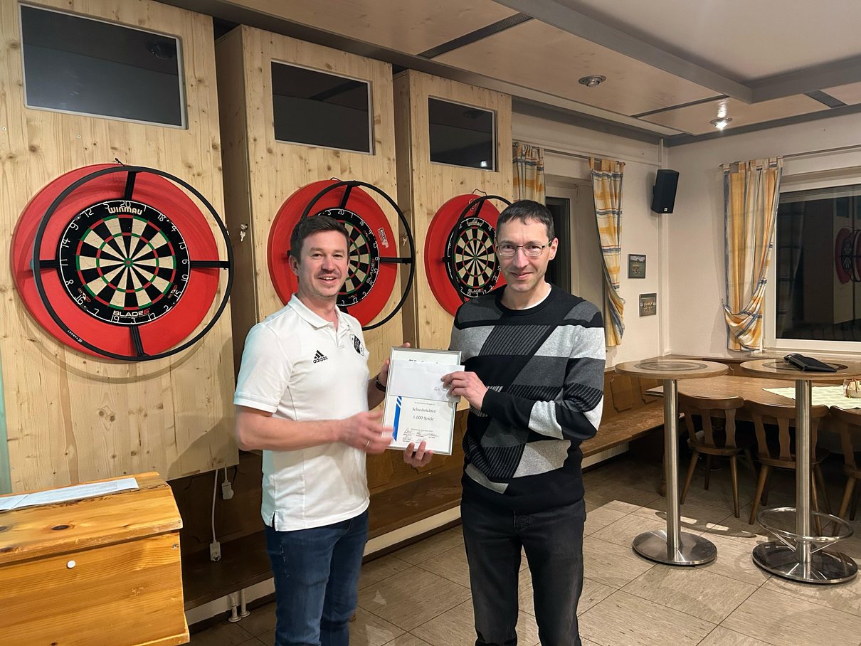 Andreas Mielich überreicht Martin Faußner eine Urkunde vor den Dartscheiben im Sportheim