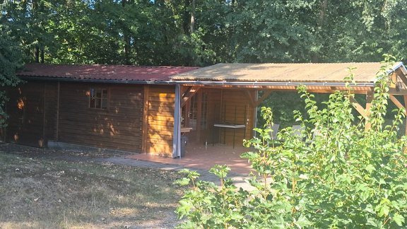 Holzhütte mit Vordach an der Tennisanlage, umgeben von Grün