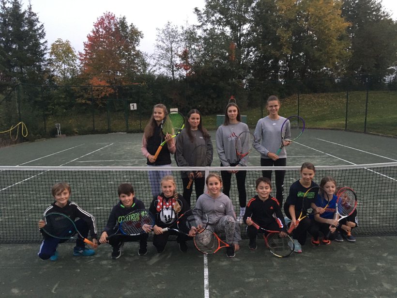 Kinder und Jugendliche mit Tennisschlägern am Netz eines Tennisplatzes