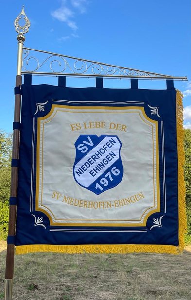 Blaue Vereinsfahne mit goldenen Fransen, in der Mitte das Wappen auf hellem Feld mit der Inschrift Es lebe der SV Niederhofen-Ehingen